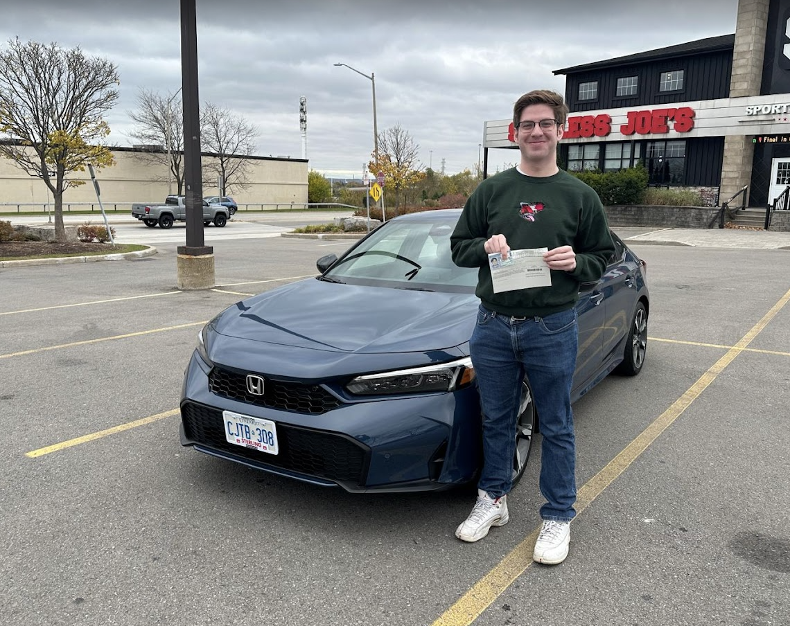 Student standing beside SteerWise car after passing G2 driving exam in Hamilton